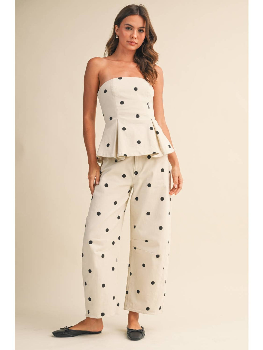 The woman is wearing a polka dot two piece set, or a polka dot co ord, with a cream background and black polka dots. 