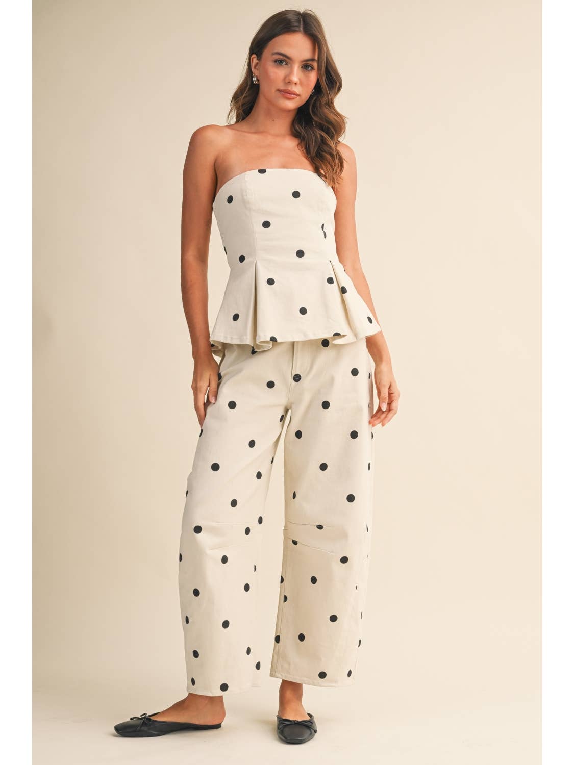 The woman is wearing a polka dot two piece set, or a polka dot co ord, with a cream background and black polka dots. 